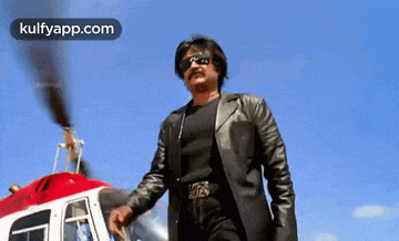 a man in a leather jacket is standing in front of a helicopter