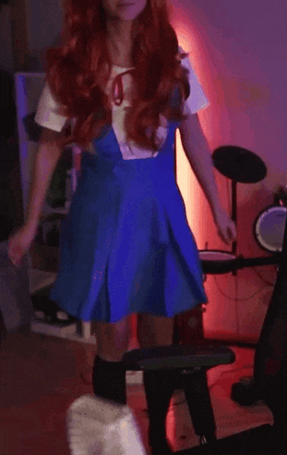 a woman with red hair and a blue dress is dancing in front of a drum set