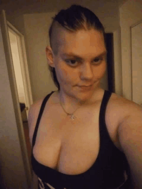 a woman with a shaved head is taking a selfie in a black tank top