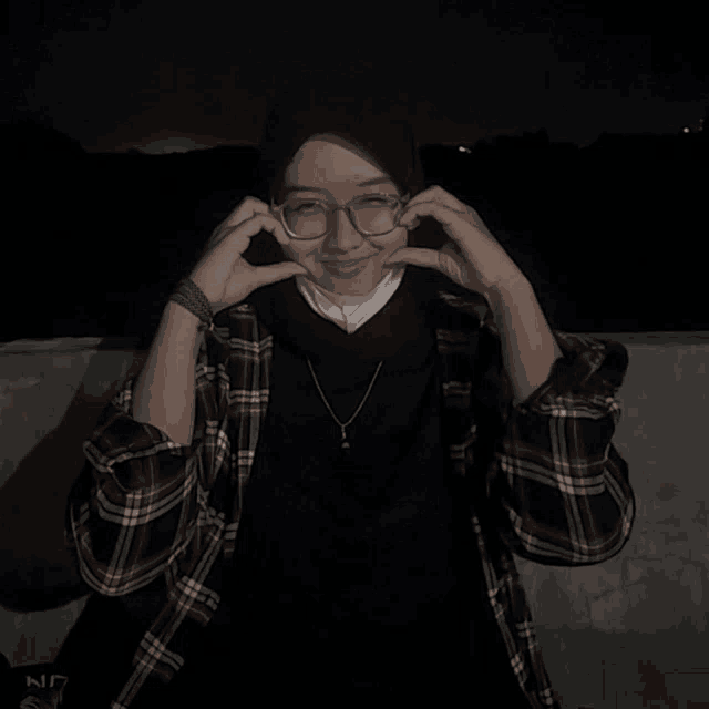 a woman wearing glasses and a plaid shirt makes a heart with her hands