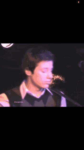 a close up of a person singing into a microphone with a purple light behind them