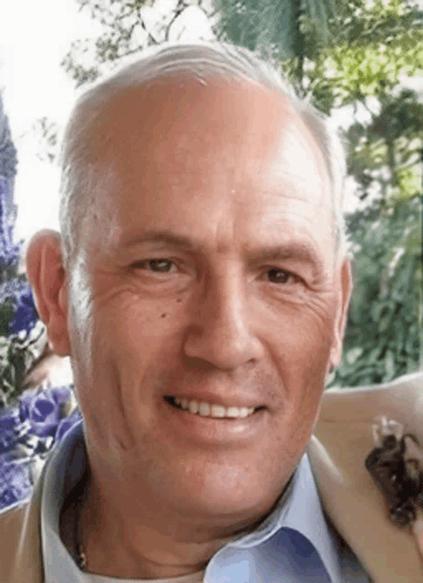 a man wearing a tan jacket and a blue shirt is smiling