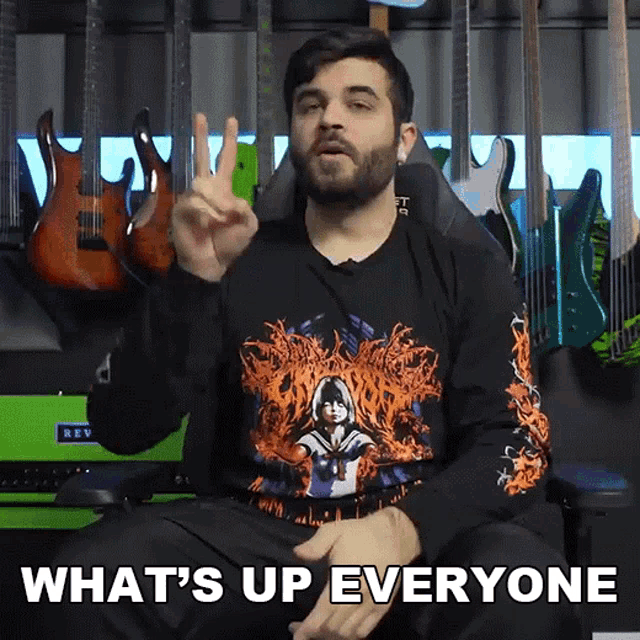 a man in a black shirt says what 's up everyone in front of a bunch of guitars