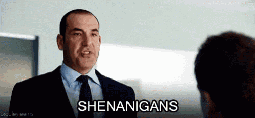 a man in a suit and tie is talking to another man and says shenanigans .