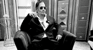 a man in a suit is sitting in a chair with his arm on his shoulder .