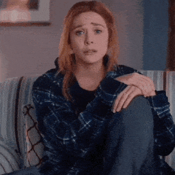 a woman in a plaid shirt is sitting on a couch with her hands on her knees .