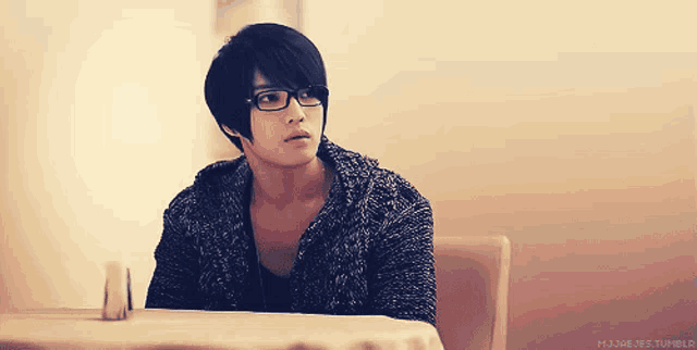 a young man wearing glasses is sitting at a table with a tumblr logo in the corner