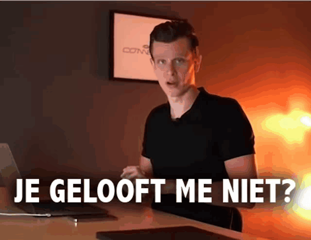 a man in a black shirt is sitting at a desk with a laptop and the words je gelooft me niet behind him