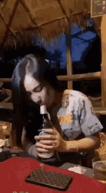 a woman is sitting at a table drinking a bottle of beer .