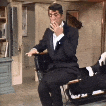 a man in a tuxedo is sitting on a chair smoking a cigarette