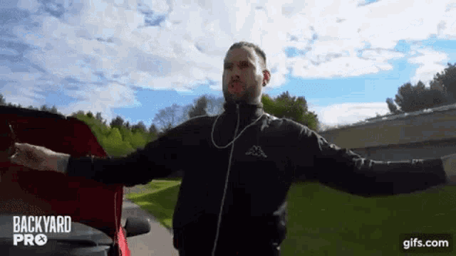 a man is standing next to a red car with his arms outstretched and a hood open .