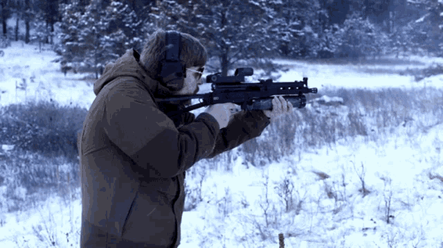 a man wearing ear muffs is holding a gun in a snowy field