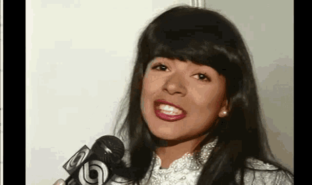 a woman with long black hair is holding a microphone and smiling .