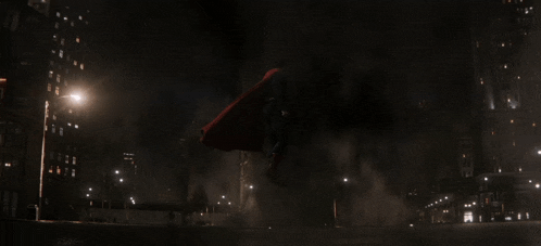 a man in a red cape is walking through a dark city