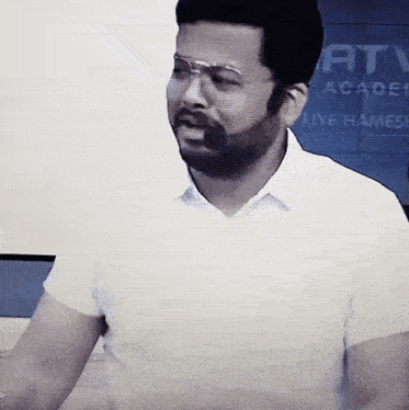 a man with a beard wearing glasses and a white shirt is standing in front of a projection screen .