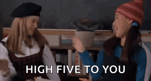 two girls are giving each other a high five while sitting next to each other in a library .