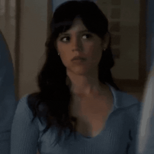 a woman in a blue shirt is standing in a dark room looking at the camera .