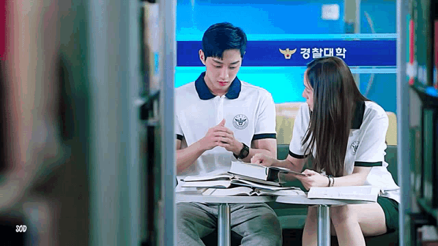 a man and a woman are sitting at a table reading books in front of a sign that says police