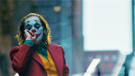 a man dressed as the joker is smoking a cigarette while standing on a city street .
