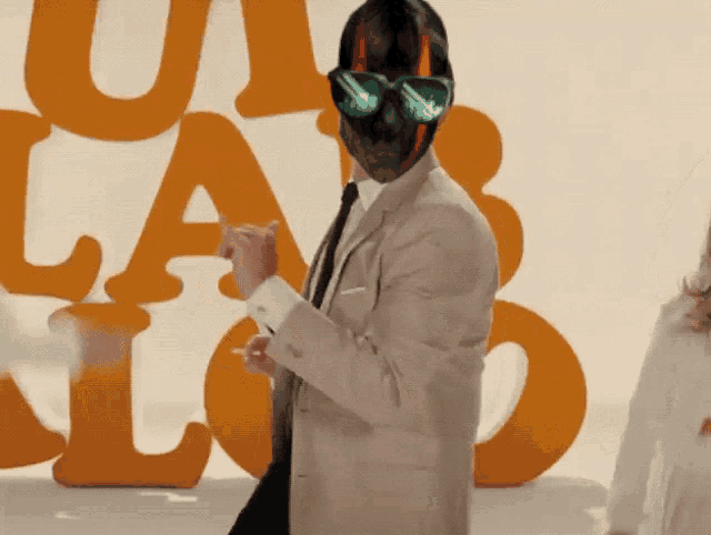 a man wearing a mask and sunglasses is standing in front of a wall of letters
