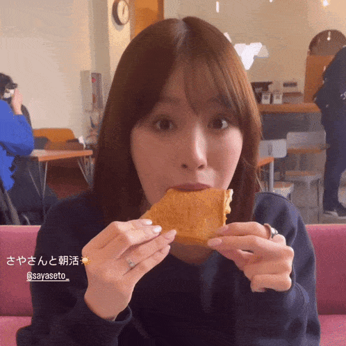 a woman sitting on a pink couch eating a piece of food that says sayaseto