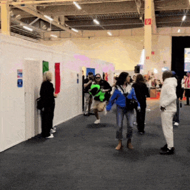 a group of people are walking in a hallway with a red exit sign