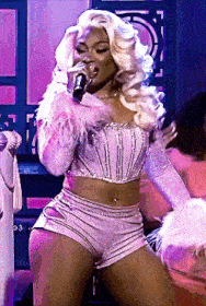 a woman is singing into a microphone while wearing a crop top and shorts .