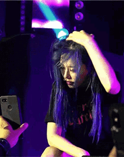 a person taking a picture of a woman with blue hair with a phone in the background
