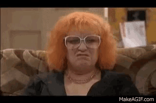 a woman with red hair and glasses is sitting on a couch .