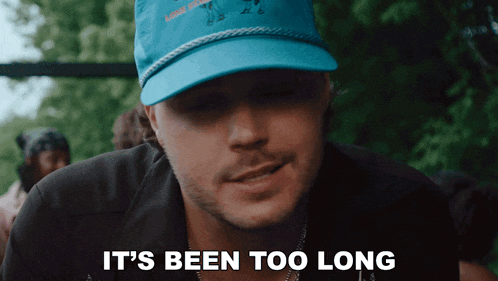 a man wearing a blue hat with the words it 's been too long below him