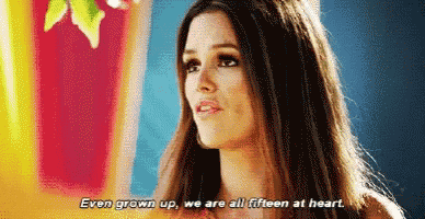 a woman with long hair is standing in front of a colorful wall and says even grown up we are all fifteen at heart .