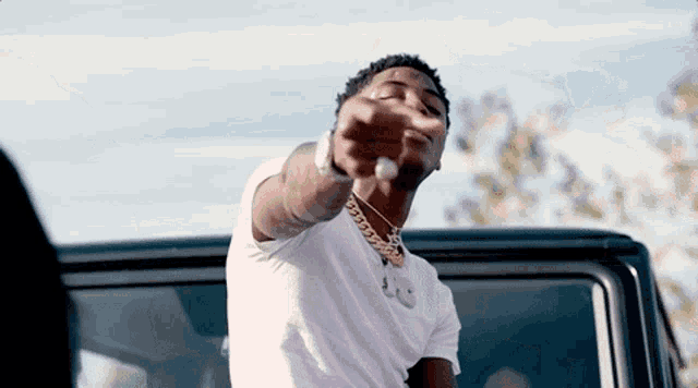 a man wearing a white shirt and a gold chain is pointing