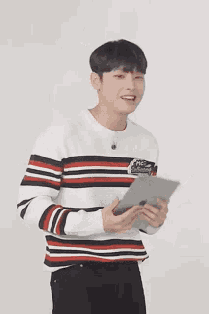 a young man wearing a striped sweater is holding a tablet