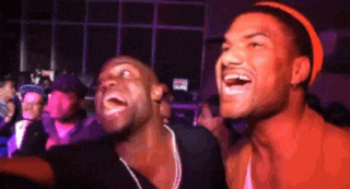 two men are laughing in front of a crowd in a dark room