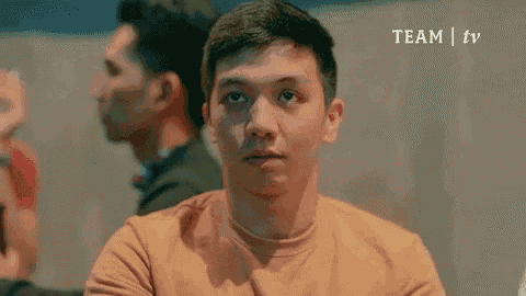 a man in an orange shirt is sitting at a table with his eyes closed and his mouth open .