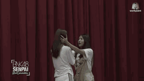 two girls are hugging in front of a red curtain with bnk48 senpai 2nd generation written on it