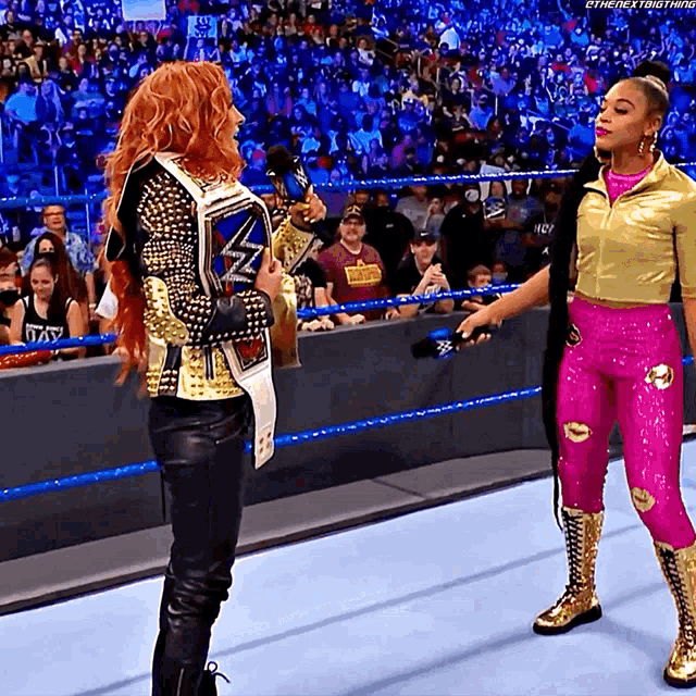 a woman in a pink outfit is holding a championship belt and talking to another woman
