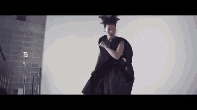 a woman in a black dress is dancing in a room with a white wall .