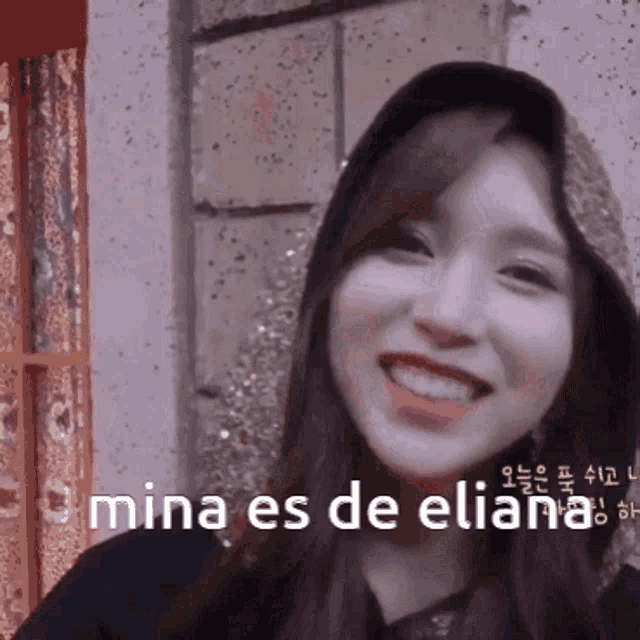 a woman wearing a hooded jacket is smiling with the words mina es de eliana written below her