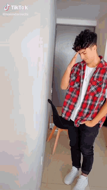 a young man in a plaid shirt and white sneakers is standing next to a chair .
