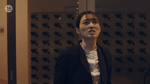 a woman in a suit stands in front of a wall with chinese characters