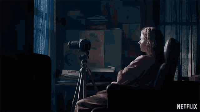 a woman is sitting in a chair with a camera on a tripod in front of her .