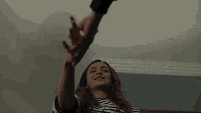 a woman in a striped shirt is reaching up towards a man 's hand