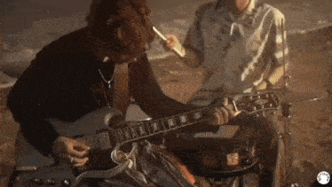 a man is playing a guitar while another man is playing drums .