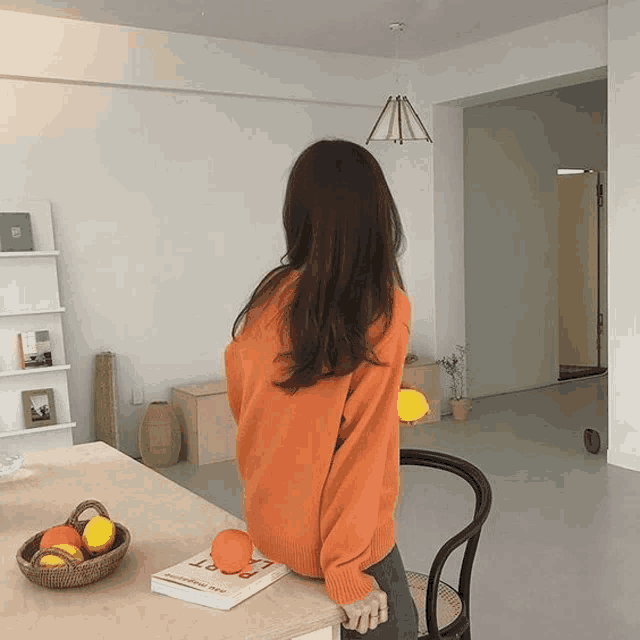 a woman in an orange sweater is standing in front of a table with a book on it that says " poetry "
