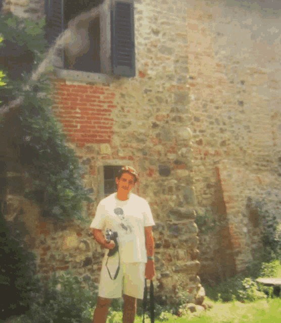 a man holding a camera stands in front of a brick wall