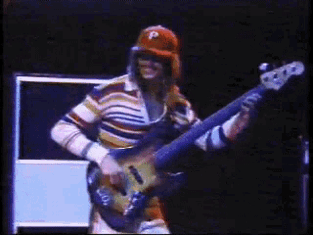 a man wearing a red hat with the letter p on it playing a guitar