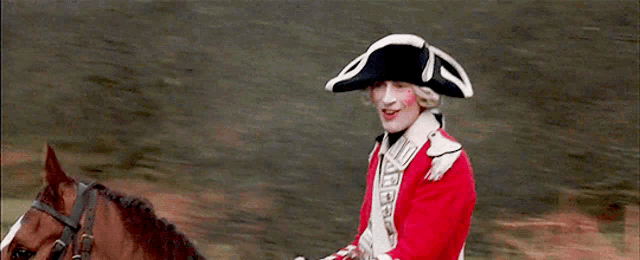 a man in a red uniform is riding a horse in a field
