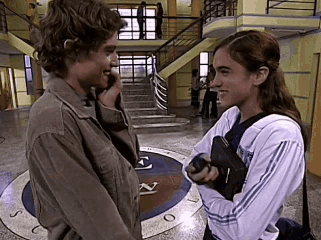 a man and a woman are standing next to each other in a hallway and talking on a cell phone .