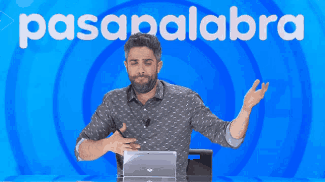 a man is sitting in front of a blue background with the word pasapalabra on it
